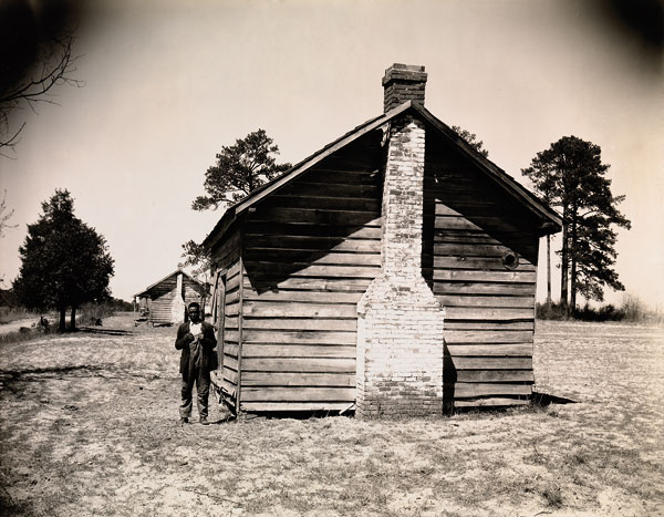 Foto Walker Evans, Man Posing for Picture in Front of Wooden House, 1936