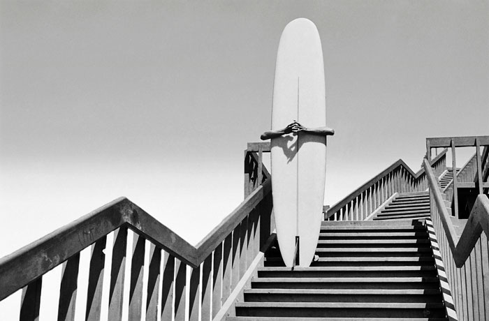 Foto Dennis Stock, Man holding a surfboard on beach steps. Corona del Mar, California, 1968